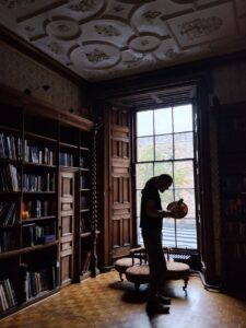 A photo of David's silhouette with a drum in an old library, surrounded by old books